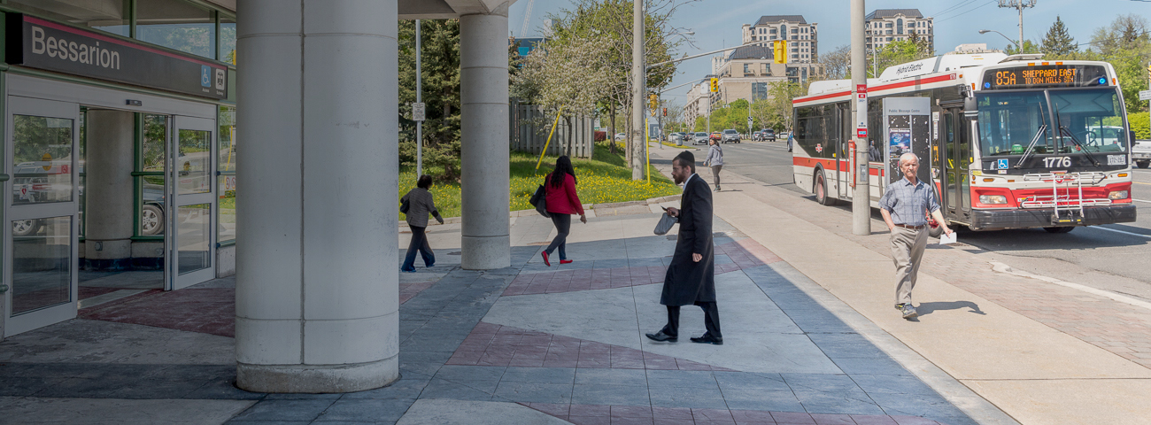 Transit Commuters walking toward waiting Bus near Bus Stop outside of Bessarion Station Entrance